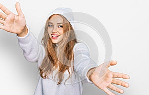 Young caucasian girl wearing wool sweater and winter cap looking at the camera smiling with open arms for hug