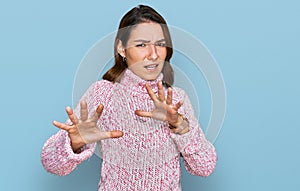 Young caucasian girl wearing wool winter sweater afraid and terrified with fear expression stop gesture with hands, shouting in