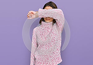 Young caucasian girl wearing wool winter sweater covering eyes with arm, looking serious and sad