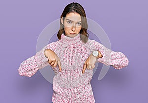 Young caucasian girl wearing wool winter sweater pointing down looking sad and upset, indicating direction with fingers, unhappy