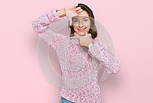 Young caucasian girl wearing wool winter sweater smiling making frame with hands and fingers with happy face