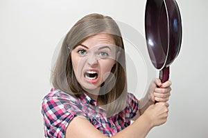 Young caucasian girl woman threaten to hit with frying pan. Angry, defensive or aggressive