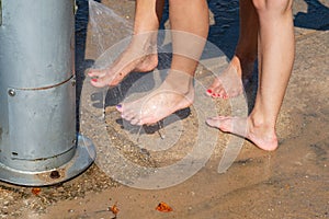 Young caucasian girls rinsing sand off their feet with a jet of water at foot washing station with a faucet
