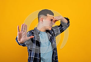 Young Caucasian guy closing his nose, suffering from awful smell, gesturing STOP on orange studio background