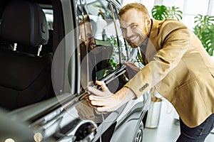 Young caucasian guy examining new car before making purchase