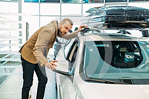 Young caucasian guy examining new car before making purchase