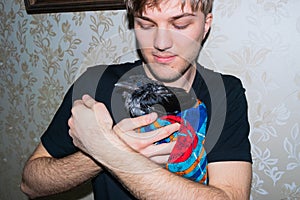 Young caucasian guy holds in his hands a wet crow cub wrapped in a cloth