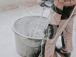 A young caucasian guy a plasterer holds a construction electric mixer and stirs dry putty with water