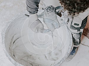 A young caucasian guy a plasterer holds a construction electric mixer and stirs dry putty with water