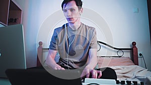 Young caucasian guy sitting in his bedroom and playing on MIDI keyboard or synthesiser and making electronic music.Dj