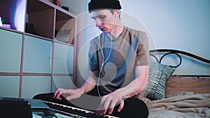 Young caucasian guy sitting in his bedroom and playing on MIDI keyboard or synthesiser and making electronic music.Dj