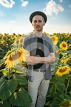 young caucasian guy straightens black hat in a sunflower field on a sunny day