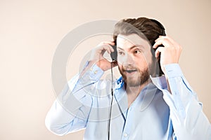 Young caucasian handsome man with a beard  putting on black headphones, wearing a blue shirt on gray