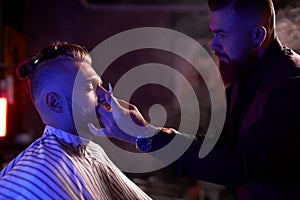 Young caucasian handsome man on chair of barber having procedure of shaving