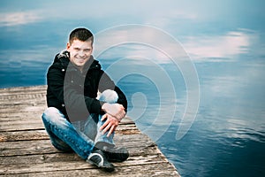 Young Caucasian Handsome Man Sitting On Wooden Pier In Spring Or