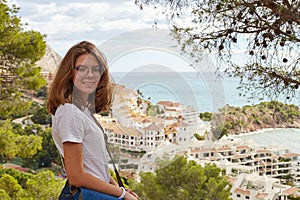 Young Caucasian happy girl stands on a hill and looks at us, against the background of the Mediterranean coast and mountain