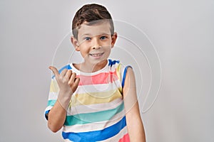 Young caucasian kid getting vaccine showing arm with band aid pointing thumb up to the side smiling happy with open mouth