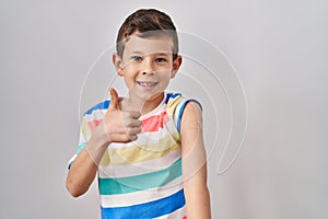 Young caucasian kid getting vaccine showing arm with band aid smiling happy and positive, thumb up doing excellent and approval