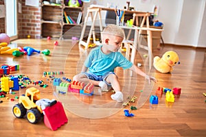 Young caucasian kid playing at kindergarten with toys. Preschooler boy happy at playroom