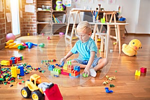 Young caucasian kid playing at kindergarten with toys. Preschooler boy happy at playroom