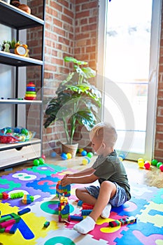 Young caucasian kid playing at kindergarten with toys. Preschooler boy happy at playroom