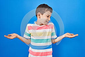 Young caucasian kid standing over blue background smiling showing both hands open palms, presenting and advertising comparison and