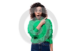 young caucasian lady with black curls dressed in a green blouse points her finger in surprise