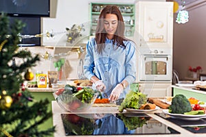 Young Caucasian lady cooking New Year or Christmas meal in decorated kitchen at home