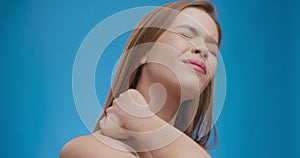 Young caucasian lady suffering from acute neck pain, massaging and stretching sore muscles, blue background