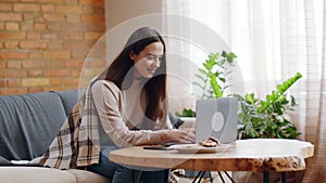 Young caucasian lady typing on laptop, chatting with friends in internet, sitting alone at home, slow motion