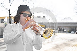 Young caucasian long-haired man in shirt and sunglasses playing trumpet outdoor