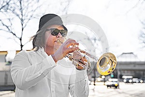 Young caucasian long-haired man in shirt and sunglasses playing trumpet outdoor