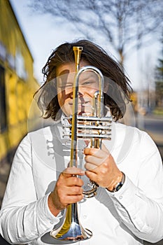 Young caucasian male cheerful jazzman looking through trumpet on sunny street