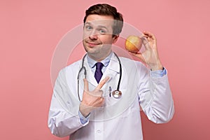 Young caucasian male doctor holding fresh apple pointing on it. Healthy diet concept