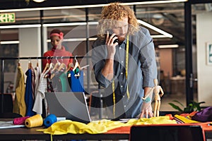 Young caucasian male fashion designer talking on smart phone while working in creative office