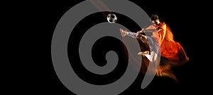 Young caucasian male football or soccer player kicking ball for the goal in mixed light on dark background. Concept of