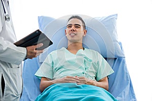 Young caucasian male patient on bed talking to doctor in hospital room