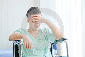 Young Caucasian male patient having headache,sitting on wheelchair in the hospital room