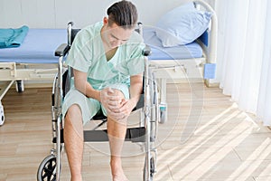 Young Caucasian male patient having knee pain,sitting on wheelchair in the hospital