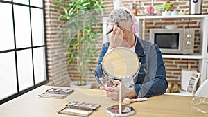 Young caucasian man applying make up listening to music at dinning room