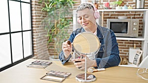 Young caucasian man applying make up listening to music at dinning room