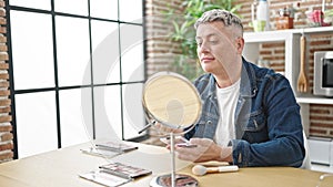 Young caucasian man applying make up sitting on table at dinning room