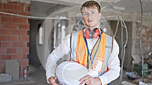 Young caucasian man architect standing with relaxed expression holding hardhat at construction site