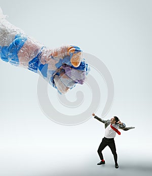 Young caucasian man avoiding big plastic hand on white studio background