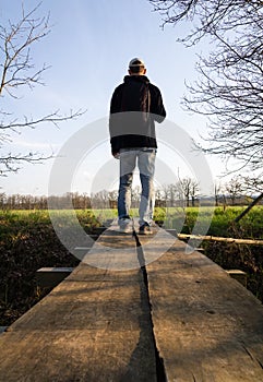 Young caucasian man from back with backpack walking on wood bridge in czech spring landscape