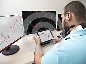 Young caucasian man in a blue shirt sitting with a table and a computer with 3 monitors doing trading