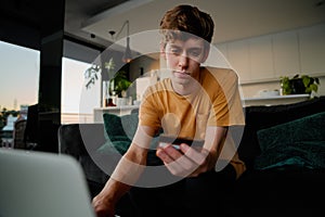 Young caucasian man in casual clothing holding credit card while using laptop at home