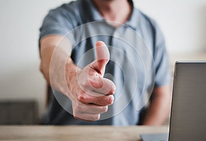 Young caucasian man in casual look sitting with laptop put on thumb up, abstract signal for approve or positive agreement.