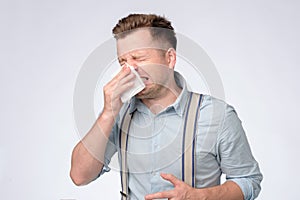 Young caucasian man covering his nose with handkerchief sneezing.