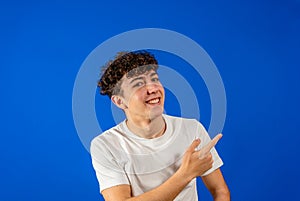 Young caucasian man with curly hair pointing smiling to the side, he is happy as he knows he is an achiever. Isolated on